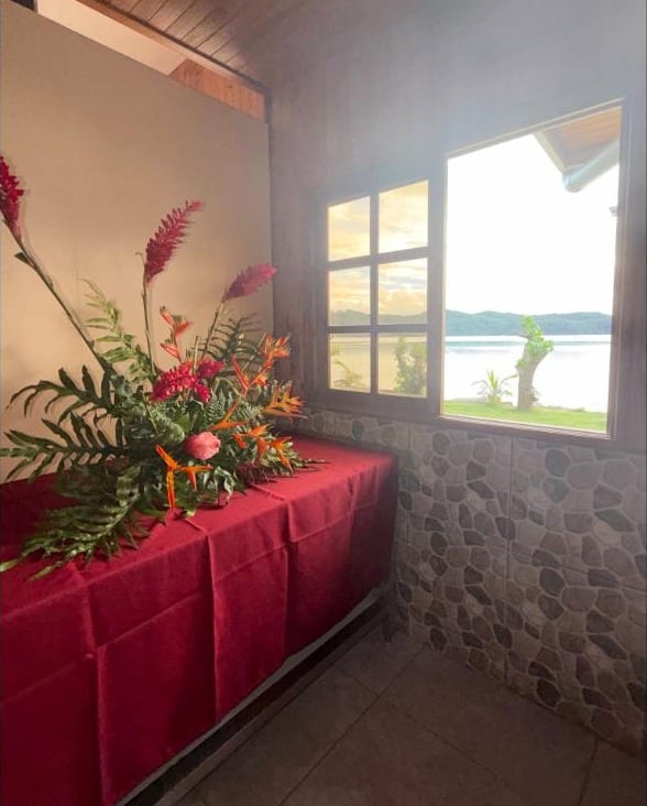 Composition de fleurs rouges devant une fenêtre ouverte sur le lagon